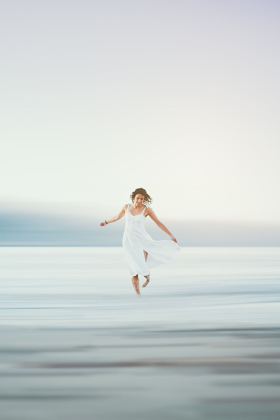 A woman in a white dress dancing on the beach