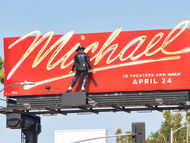 Panneau publicitaire rouge de Michael avec silhouette de Michael Jackson; texte: IN THEATERS AND IMAX APRIL 24, ciel bleu.