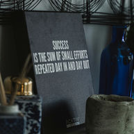 Motivational desk still life with sign reading Success is the sum of small efforts repeated day in and day out, blue vase and candle