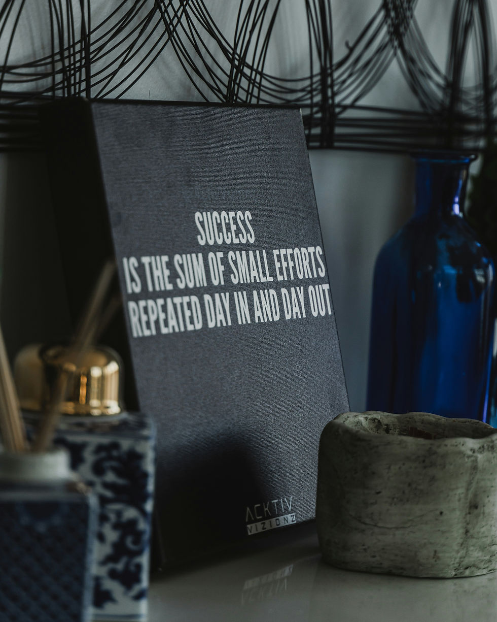 Motivational desk still life with sign reading Success is the sum of small efforts repeated day in and day out, blue vase and candle