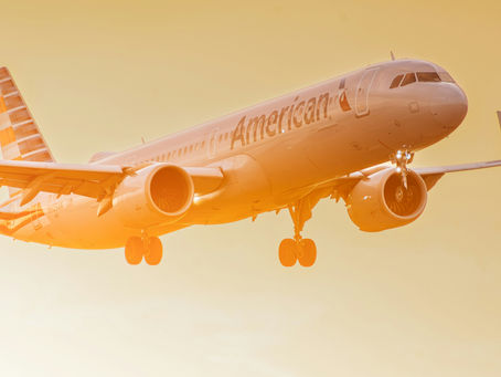 Airplane flying in a warm orange sky, displaying "American" on the side. Sunlight creates a bright atmosphere with glowing tones.
