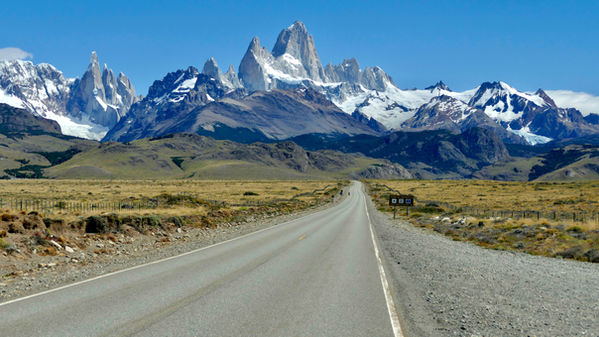 Strada deserta che conduce verso le vette spettacolari del Monte Fitz Roy sotto un cielo azzurro in Argentina.