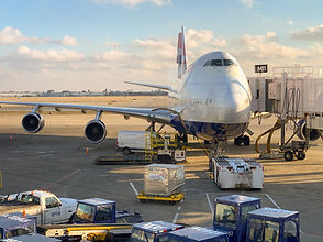 A large British Airways Boeing 747 is parked at a tarmac gate, with various support vehicles and equipment around it.
