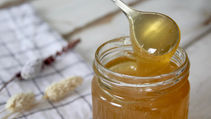 A spoonful of honey over a jar of honey, sitting on a table.