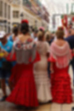 Crowd in flamenco dresses with flower hairpieces walks down a festooned shopping street, Beshka sign visible.