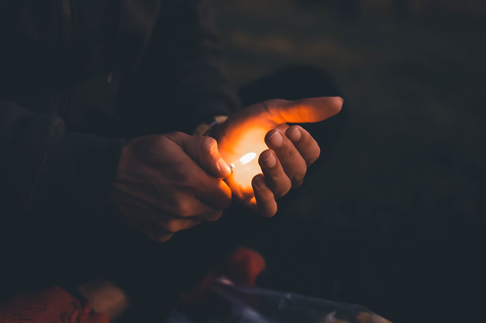 Hands in darkness cup a glowing lighter flame, casting warm orange light in a moody close-up.