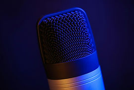 Close-up of a microphone illuminated by blue light against a dark background, highlighting its mesh pattern and metallic details.