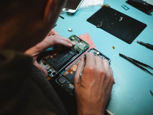 Person repairing a smartphone on a blue table with tools and parts. Focused hands, intricate circuit details, tech repair scene.