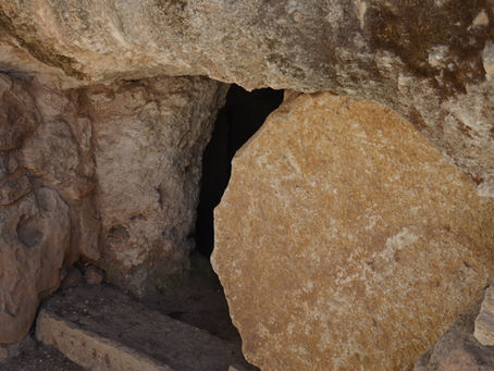 Large stone covers an entrance to a cave or tomb. The setting is rocky, with earthy tones and textures dominating the scene.