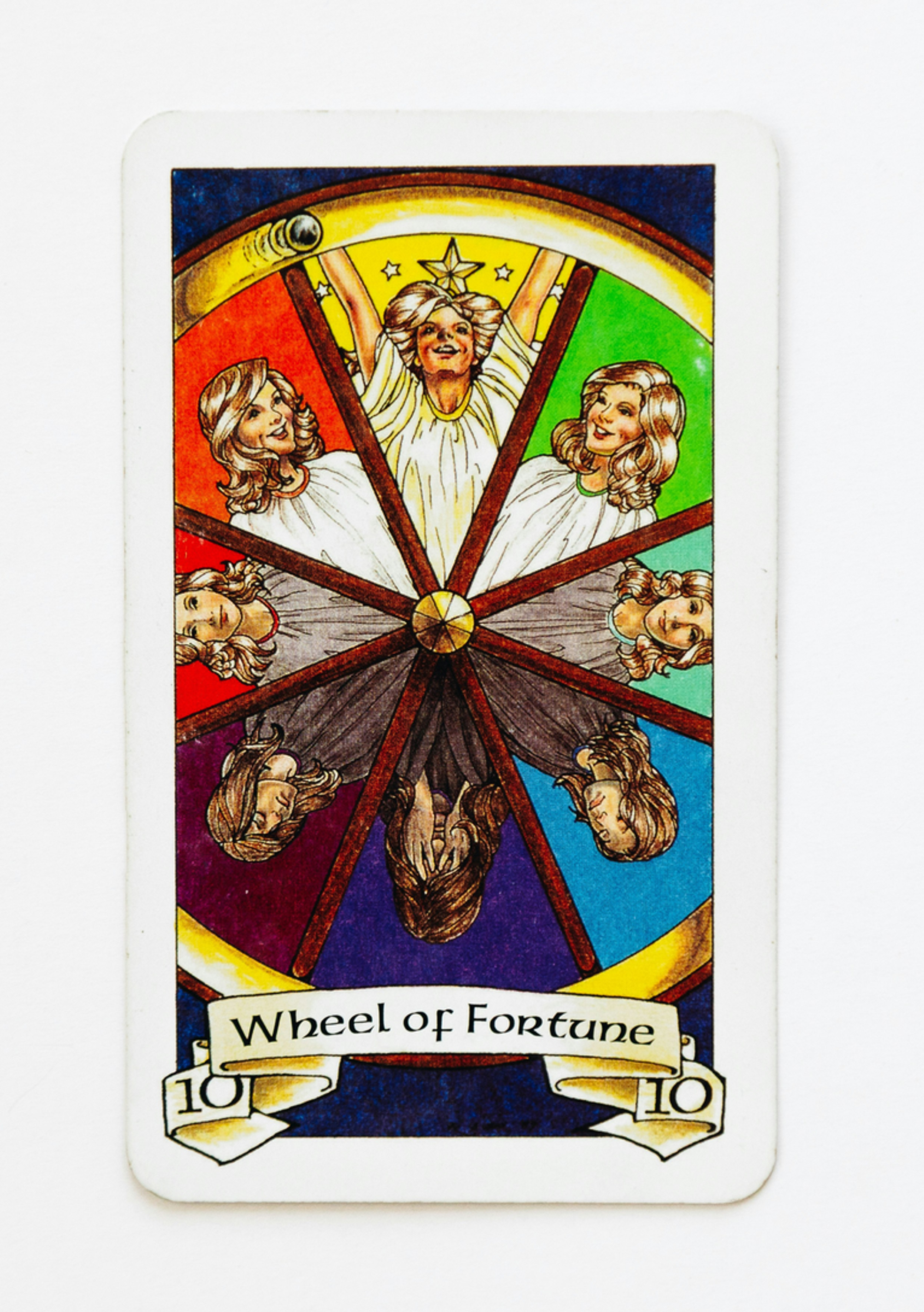 Tarot card Wheel of Fortune on a white background, showing colorful faces around a spinning wheel and the text Wheel of Fortune.