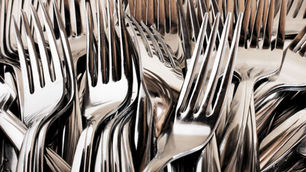 Close-up of stacked silver forks and spoons, their polished metal surfaces reflecting light in a dense abstract pattern.