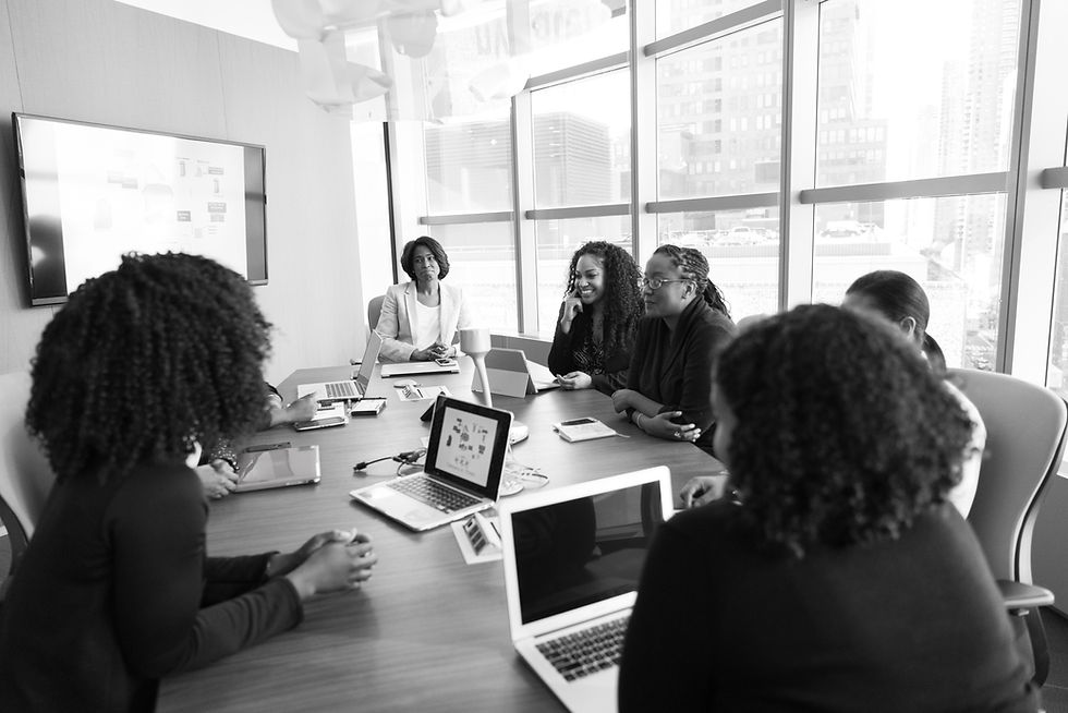 Grayscale photo of a group of individuals wearing business attire, sitting at a conference table at an office, with laptops open.