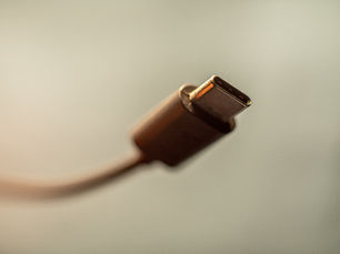 Close-up of a USB-C cable tip against a plain beige background, softly lit and slightly out of focus.
