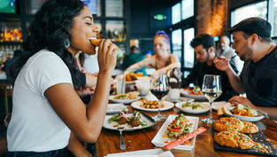 Students enjoying food and drinks at a lively restaurant in Loughborough. Warm lighting, colourful food, and a cheerful atmosphere fill the scene.
