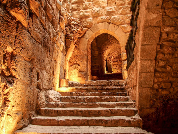 Passaggio interno in pietra del Castello di Ajlun con scale, archi e illuminazione calda.