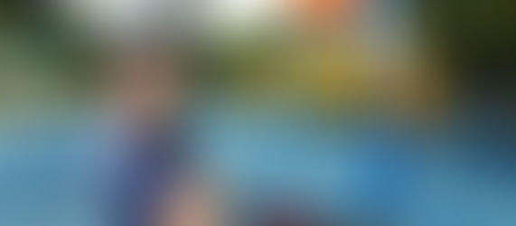 boy at a playground, sitting on a bike, wearing a bike helmet. his arms are crossed and his face is angry. 