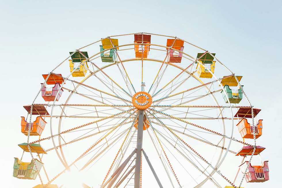 Colorful Ferris wheel with orange "Paradise Amusements" sign at center. Brightly colored cabins, clear sky, and sunlight create a joyful mood.