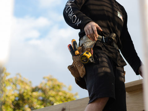 A man in a black t shirt and shorts wearing a tool belt.