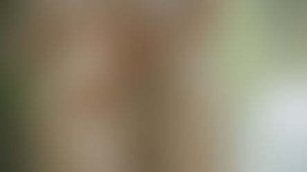 Two pregnant women in beige dresses stand outdoors by a lake, hands on their bellies, in a calm, soft-lit scene.
