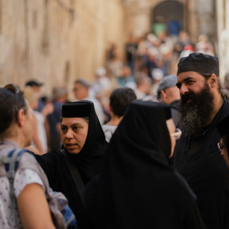Guided private tour of Old City Jerusalem. Sagi Levy Tour Guide, wearing a black kashrut and traditional beard, speaks with a tourist group on a bustling stone street in the Christian Quarter.