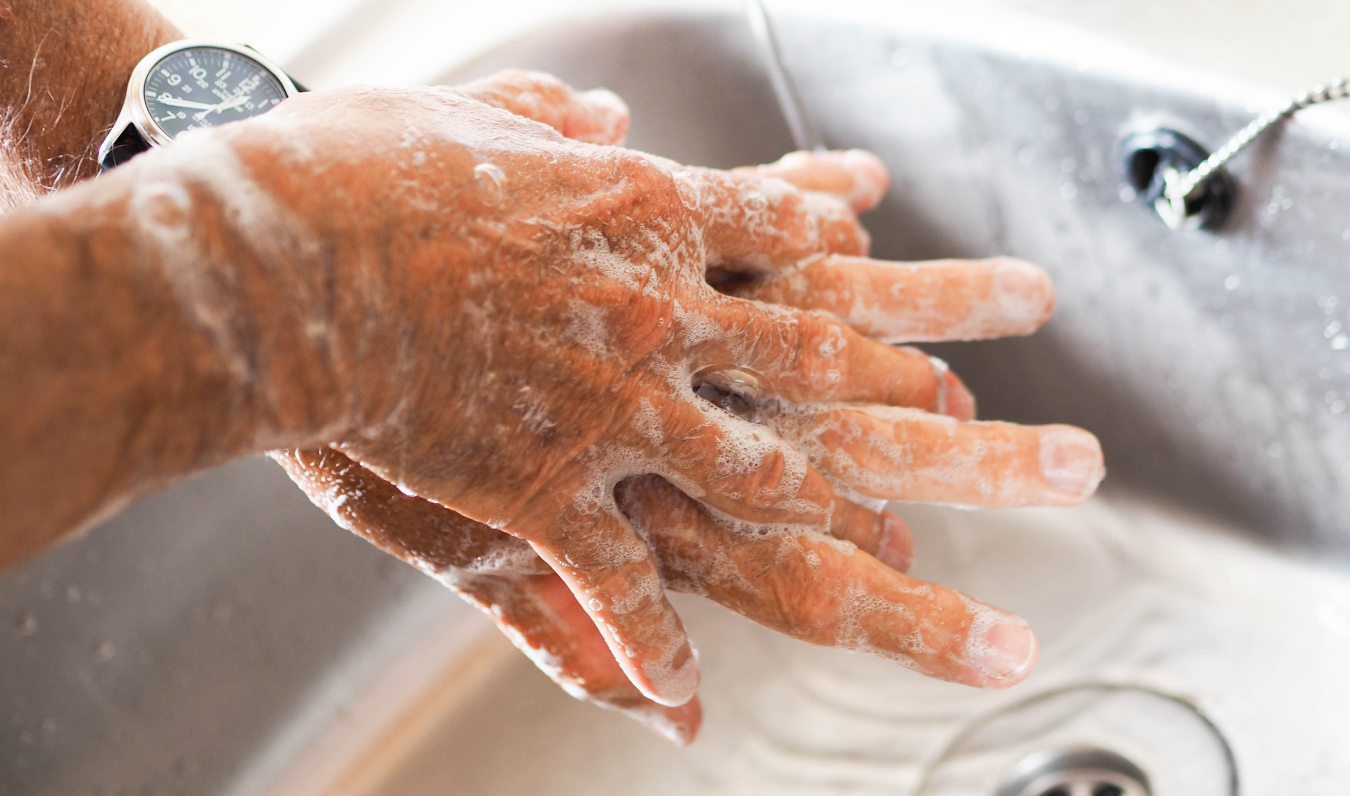 Hands covered in soap suds washing under a faucet, illustrating common hand washing compulsions in OCD.