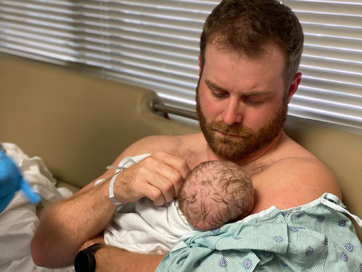 A man sits in a hospital room, cradling a baby in his arms. He looks down at the baby with a look of awe.