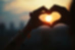 two hands forming a heart and holding them up at dusk and circleing around the sun