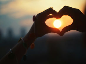 hands in the shape of a heart being held up to the setting sun