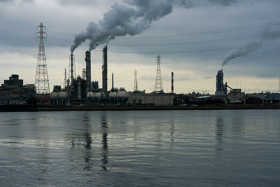 Industrial skyline with smoke rising from chimneys over a river.