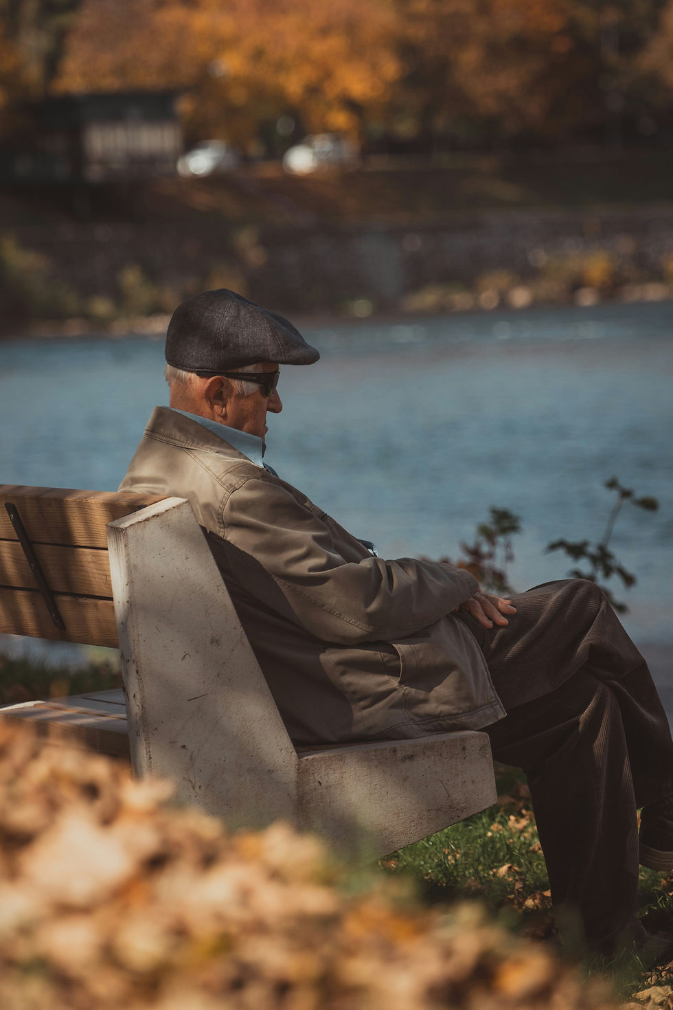 An old gentleman in a flat cap sitting on a bench by water, like Theo of Golden.