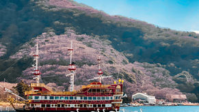 Hakone pirate ship sightseeing cruise docked in front of a mountain side pink with cherry blossoms