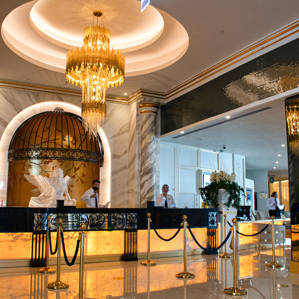 Luxurious hotel reception area with marble walls, a large golden chandelier, and staff standing behind an illuminated front desk, featuring classical statues and ornate decor