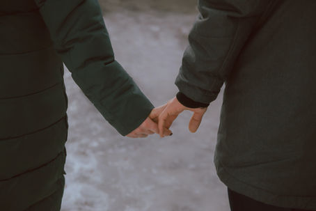 Two people reaching out and trying to hold each other’s hands, their fingers barely touching, symbolizing the struggle of letting go in a relationship.