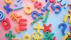 Colorful plastic letters and symbols scattered on a pink and blue background, creating a playful, آموزشی look.