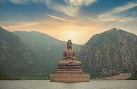 Golden-lit Buddha facing a lake with mountains, symbolising deep awareness and present-moment clarity