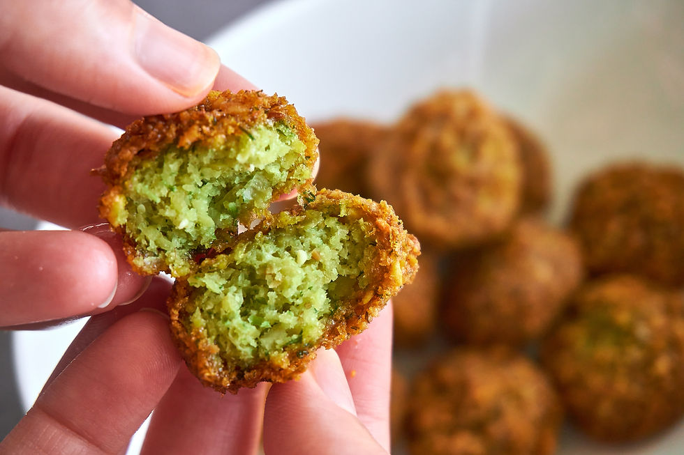 A hand holding a broken open falafel ball over a bowl of falafel balls
