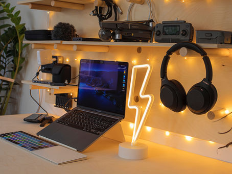 Workspace with open laptop, glowing lightning lamp, headphones, and gadgets on wooden shelves. Warm lighting and plants create a cozy vibe.