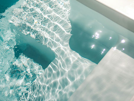 Sunlit pool steps submerged in clear blue water, creating ripples and reflections. A bright and serene atmosphere.