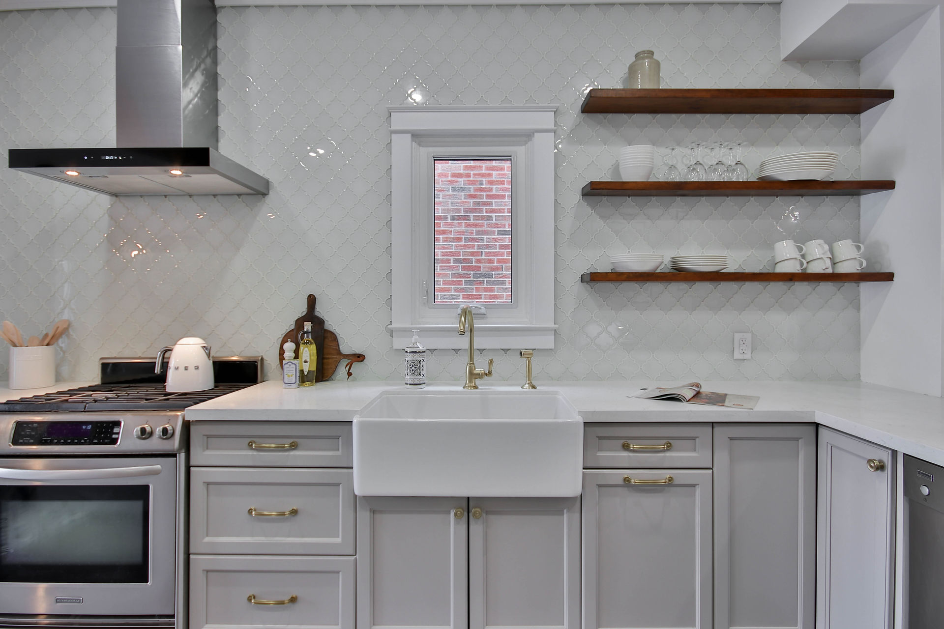 Grey framed kitchen with ceramic farmhouse style sink, shelves and tile backsplash.