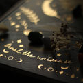 Glowing decorative card with stars, moons and dried flowers, reading trust the universe in warm light.
