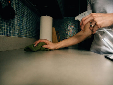 A person wiping down a kitchen counter with a cloth and spray cleaner
