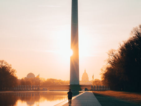 a picture of a person walking beneath the Washington monument at sunset