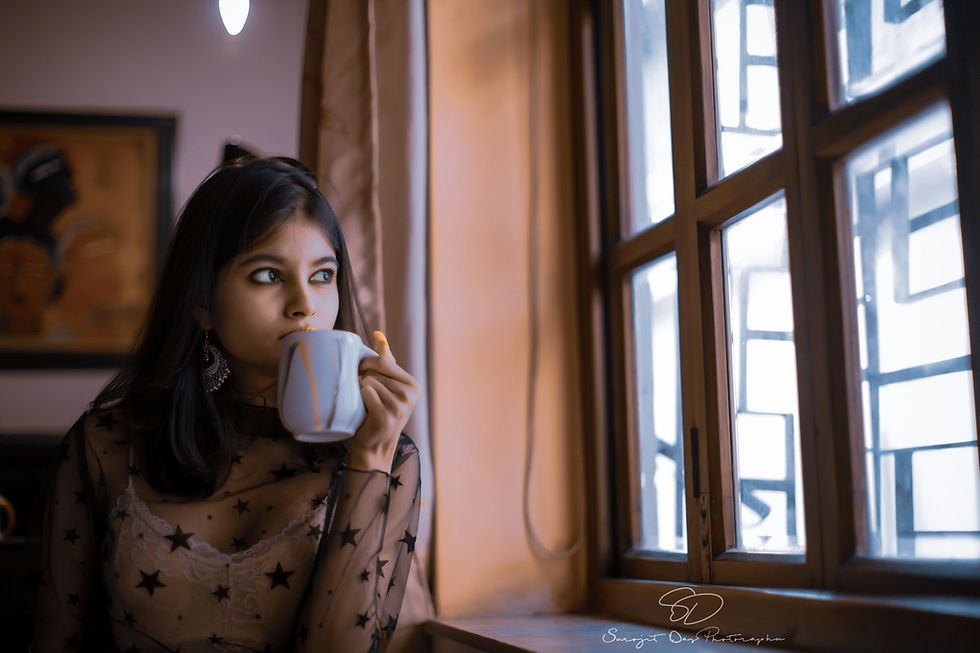 A woman holding a cup of tea by a window, thinking