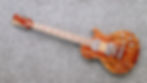 A mahogany electric guitar with a natural grain finish lies on a gray carpet. The guitar features silver hardware and visible red inlay lines.