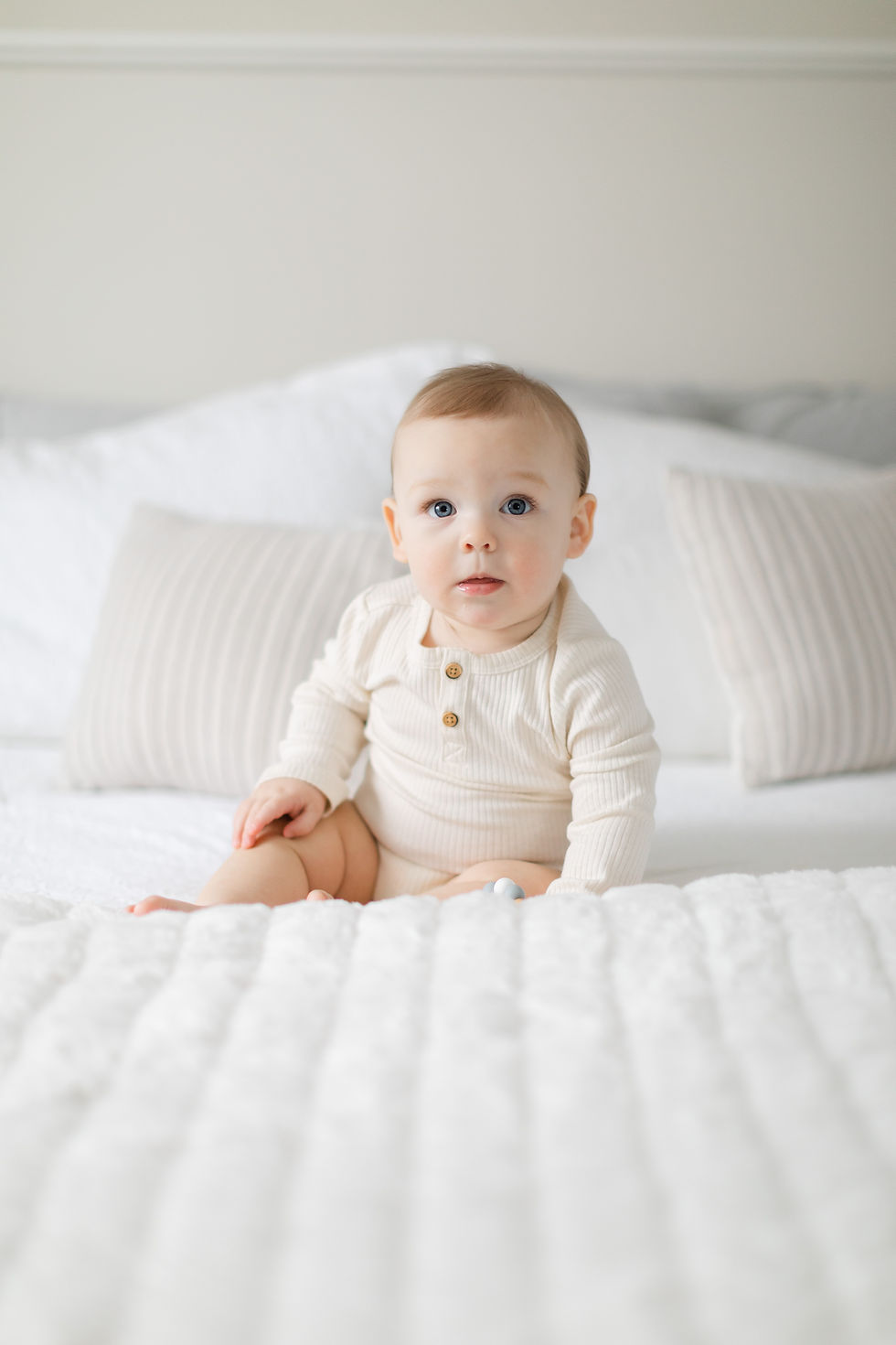Young baby sitting on a bed, facing the camera.