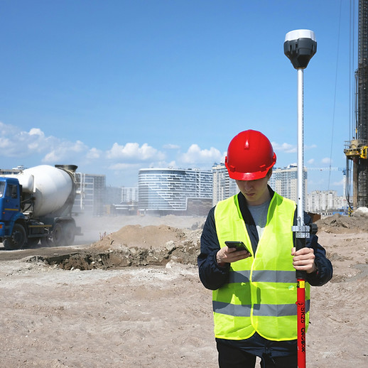 Surveyor in red hard hat using GPS equipment and phone at a construction site