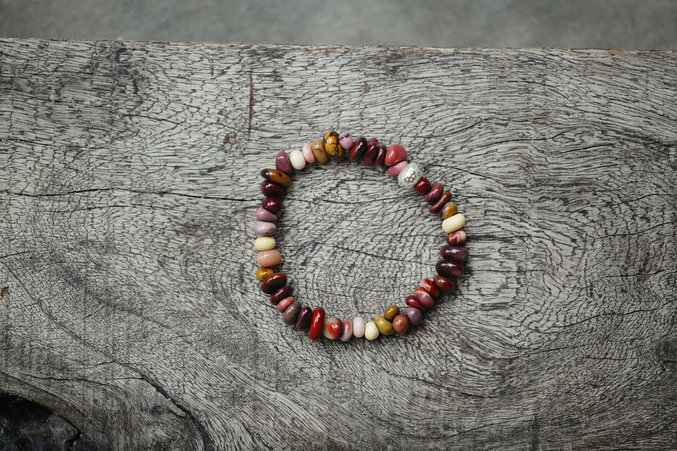 Multicolored beaded bracelet with a metal bead on textured wooden surface, displaying earthy tones and a rustic feel.