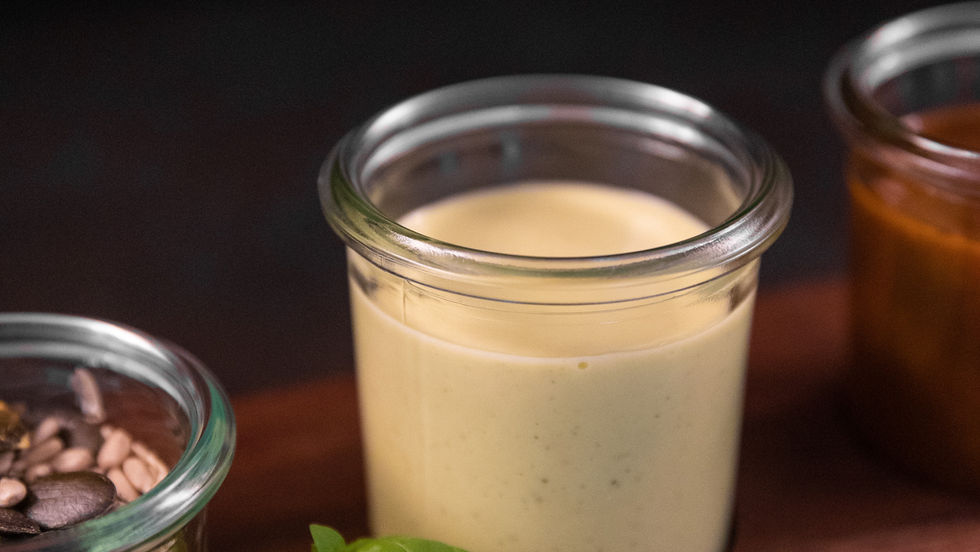 A jar of creamy homemade mayonnaise is elegantly displayed on a wooden board, accompanied by a fresh basil garnish.