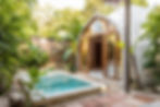 Tropical poolside setting with a dome-shaped white building and open wooden doors, surrounded by lush green plants and clear blue sky.