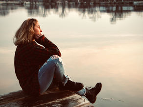 Woman sitting by a lake at sunset, lost in thought, symbolising a pause to notice what's on autopilot